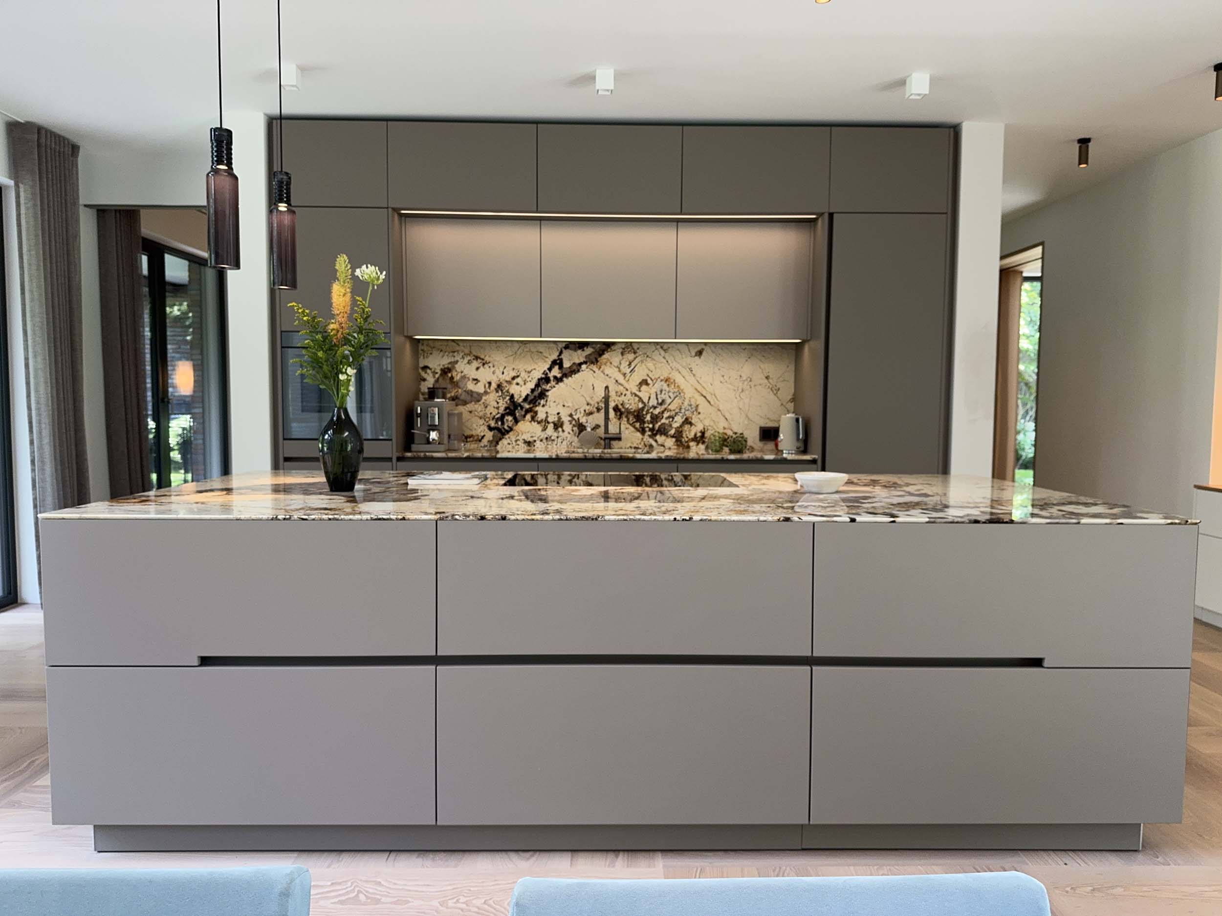 interior-design-hamburg-weisselberg-kitchen-and-interior_1 Offene Wohnküche mit grauer Kücheninsel und Rückwand aus gemasertem Naturstein